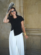 a lady wears a black top with asymmetric hem design with white loose fit pants